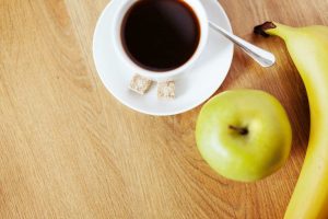 Coffee with sugar cubes, green apple, and banana on wooden table.