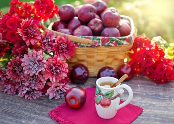 Basket of red apples with flowers and apple cinnamon tea on table.