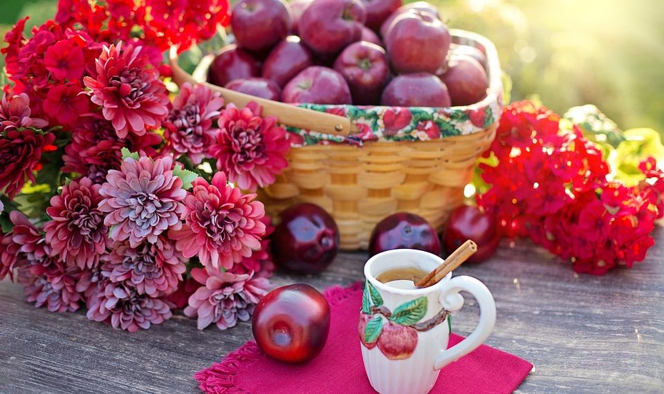 Basket of red apples with flowers and apple cinnamon tea on table.