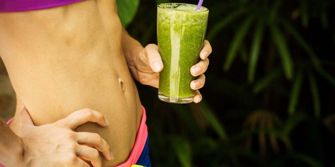 Woman holding green smoothie, focusing on fitness and health.