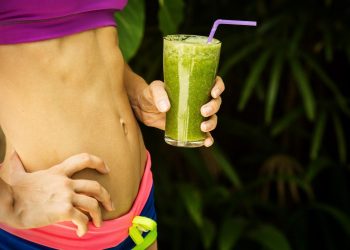 Woman holding green smoothie, focusing on fitness and health.