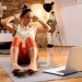 Woman doing sit-ups at home with a laptop for online workout guidance.