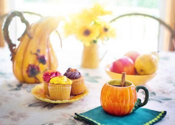 Cupcakes and apple cider on a floral table with autumn decorations.