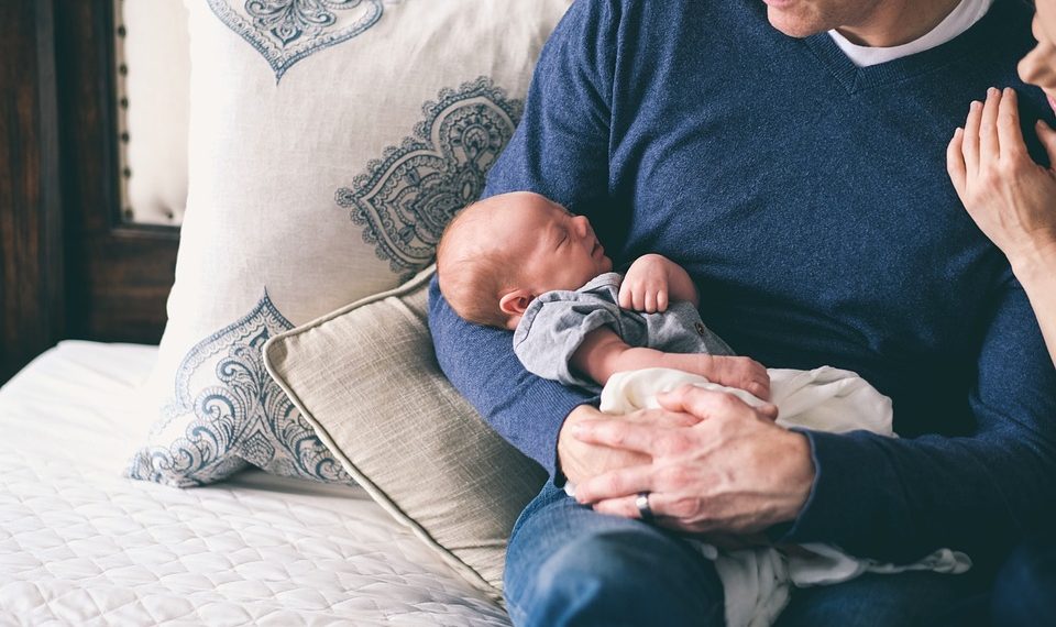 Father holding newborn baby while mother touches his shoulder.