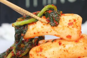 Chopsticks holding spicy Korean rice cakes with greens.