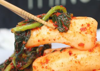 Chopsticks holding spicy Korean rice cakes with greens.