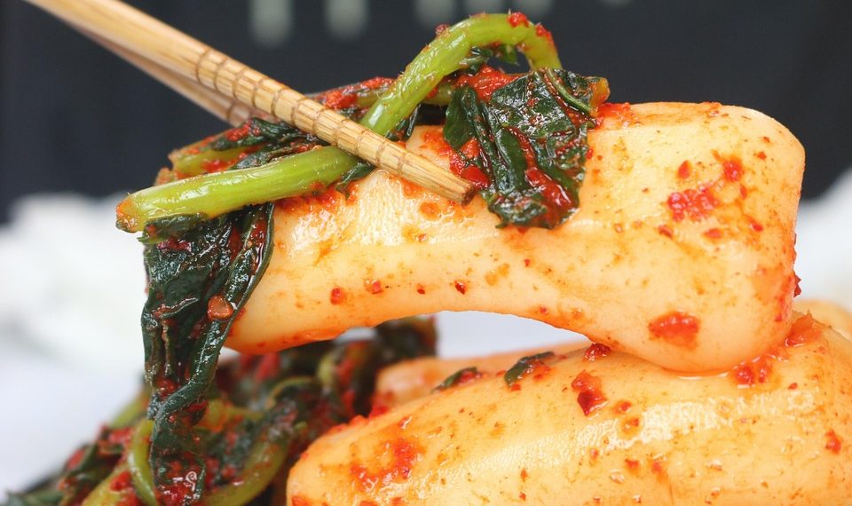 Chopsticks holding spicy Korean rice cakes with greens.