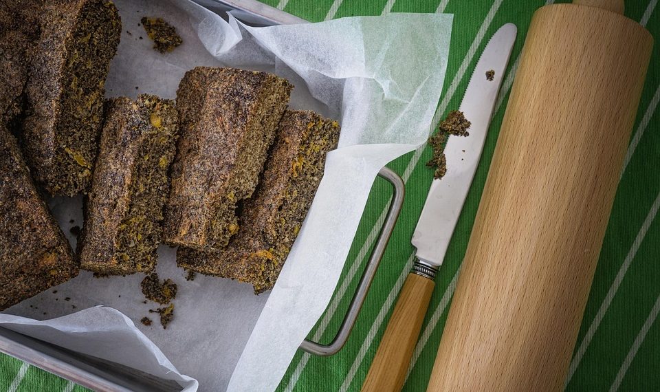 Homemade poppy seed bread arranged on parchment paper with a knife and rolling pin.