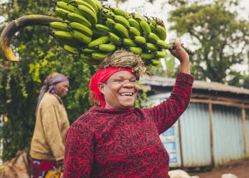 Woman joyfully carrying a bunch of bananas on her head.