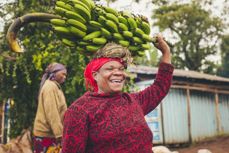 Woman joyfully carrying a bunch of bananas on her head.