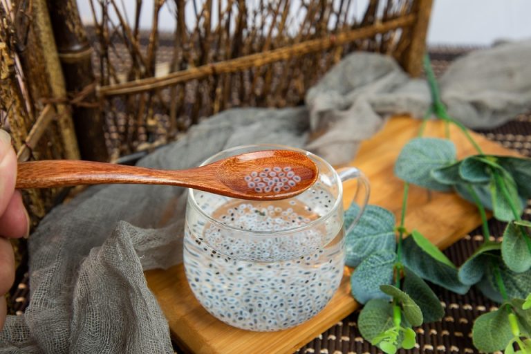 Spoon with chia seeds over glass cup on wooden tray.