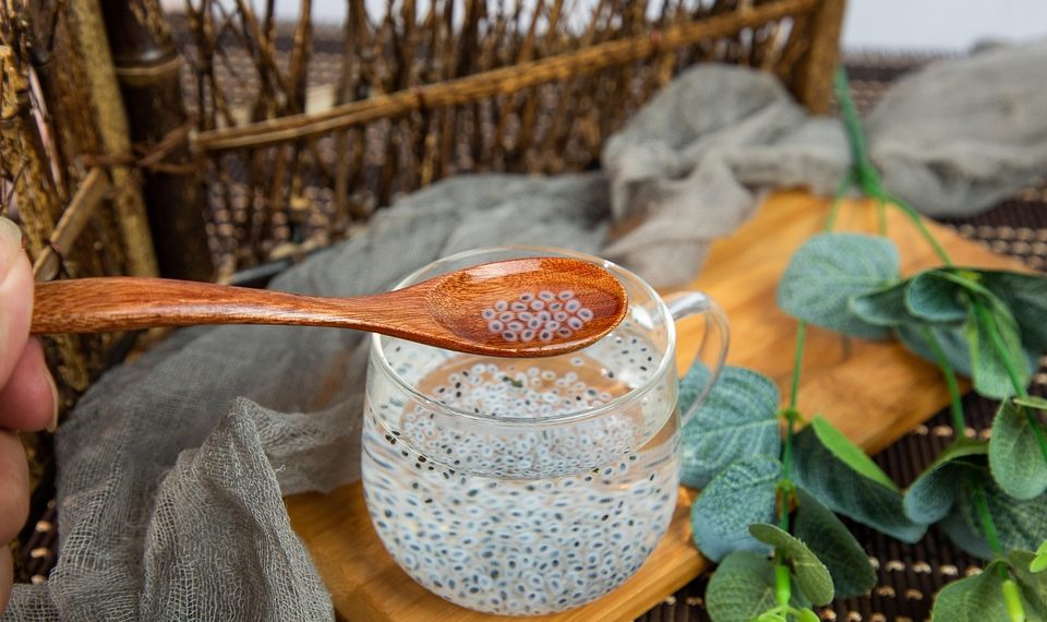 Spoon with chia seeds over glass cup on wooden tray.