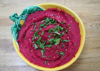 Beetroot hummus garnished with sesame seeds and cilantro in a decorative bowl.
