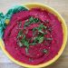 Beetroot hummus garnished with sesame seeds and cilantro in a decorative bowl.