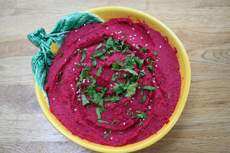 Beetroot hummus garnished with sesame seeds and cilantro in a decorative bowl.