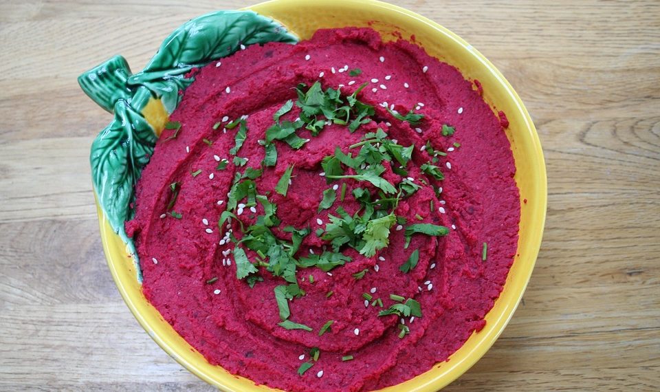 Beetroot hummus garnished with sesame seeds and cilantro in a decorative bowl.