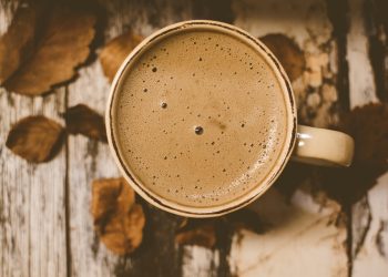 Creamy coffee in a mug with autumn leaves on wooden table.