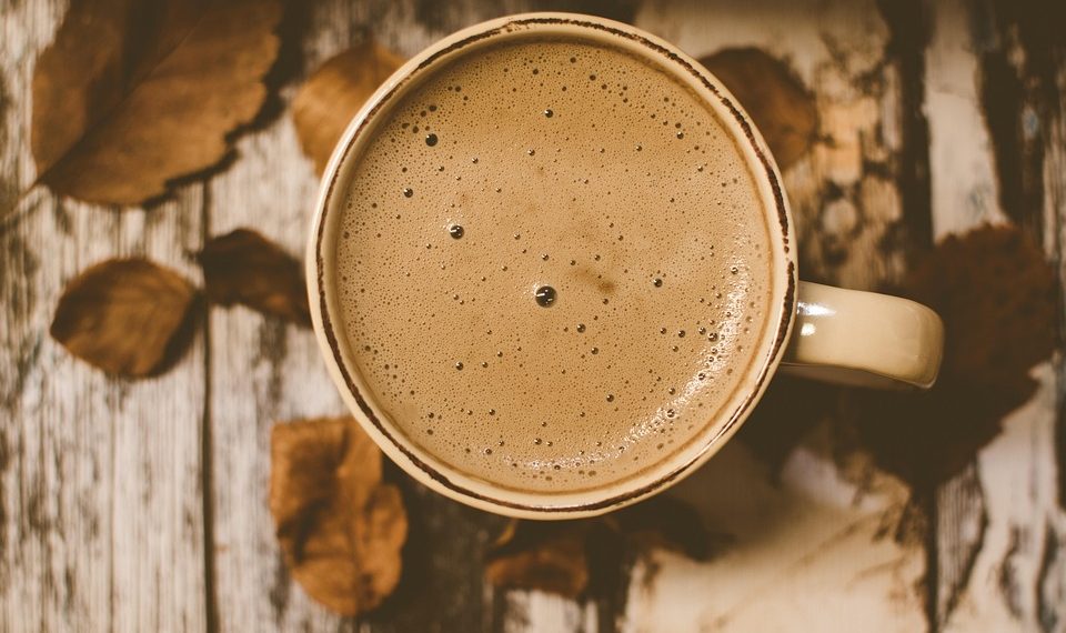 Creamy coffee in a mug with autumn leaves on wooden table.
