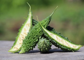 Bitter gourd cut open on wooden table with blurred green background.