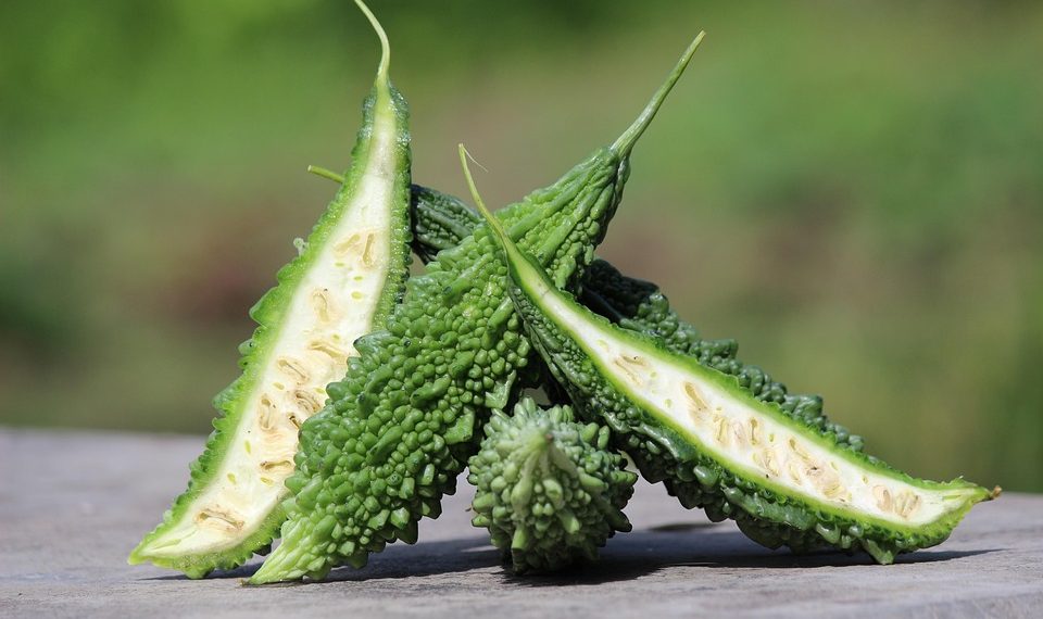 Bitter gourd cut open on wooden table with blurred green background.