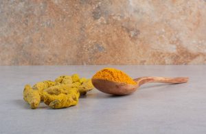 Turmeric roots and powder on a wooden spoon on a marble surface.