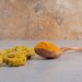 Turmeric roots and powder on a wooden spoon on a marble surface.