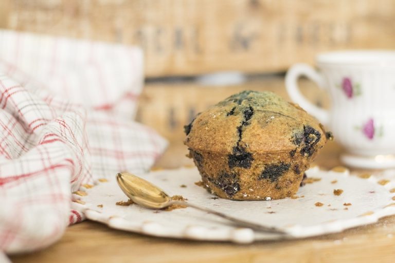 Blueberry muffin with a gold spoon on a napkin by a teacup.