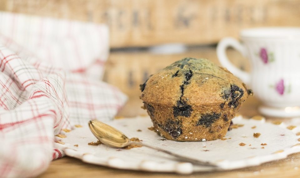 Blueberry muffin with a gold spoon on a napkin by a teacup.