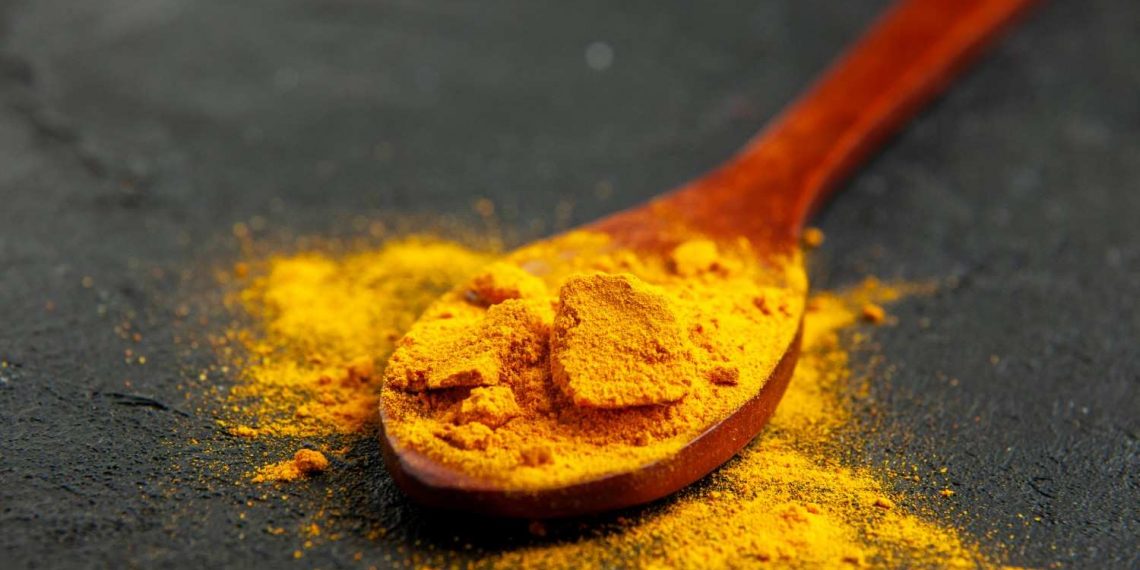 Wooden spoon with vibrant turmeric powder on a dark surface.