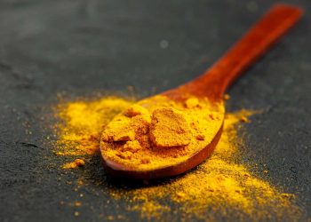 Wooden spoon with vibrant turmeric powder on a dark surface.