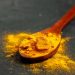 Wooden spoon with vibrant turmeric powder on a dark surface.