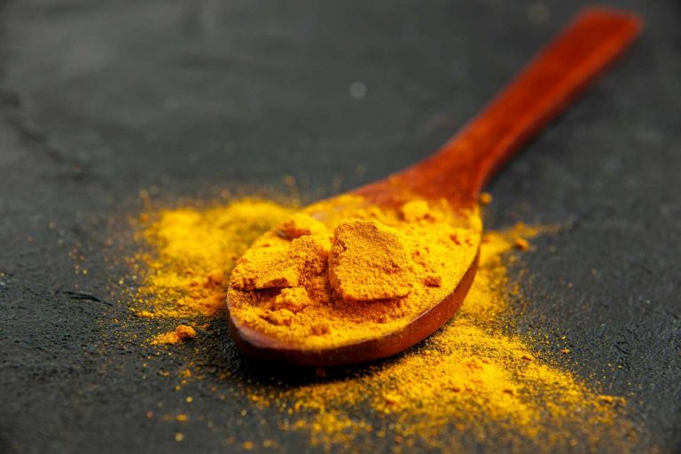 Wooden spoon with vibrant turmeric powder on a dark surface.