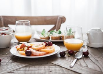 Plate with fresh fruit and juice on breakfast table.