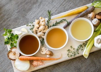 Herbal broths in bowls with fresh vegetables and herbs.
