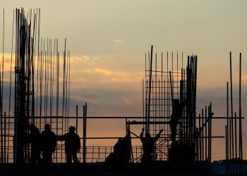 Construction workers building structure at sunset.