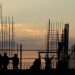 Construction workers building structure at sunset.