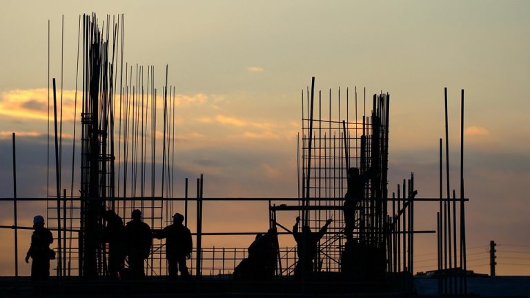 Construction workers building structure at sunset.