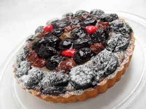 Mixed berry tart topped with powdered sugar on a clear plate.