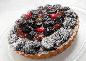 Mixed berry tart topped with powdered sugar on a clear plate.
