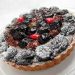 Mixed berry tart topped with powdered sugar on a clear plate.