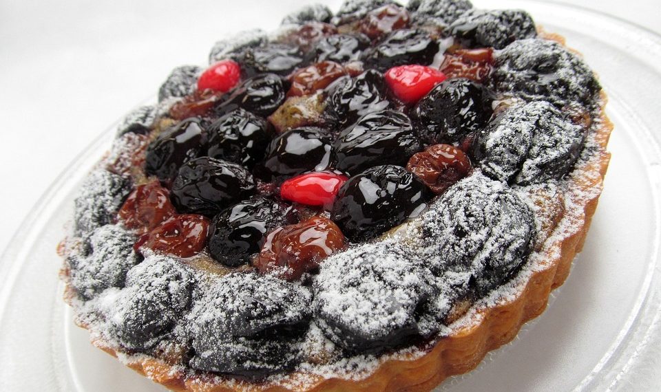 Mixed berry tart topped with powdered sugar on a clear plate.