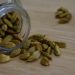 Green cardamom pods spilling from a glass jar on a wooden surface.
