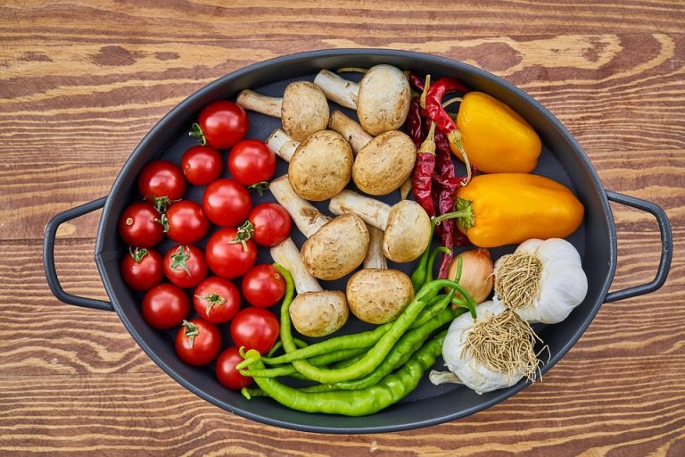 Fresh vegetables like tomatoes, mushrooms, and peppers in an oval pot.