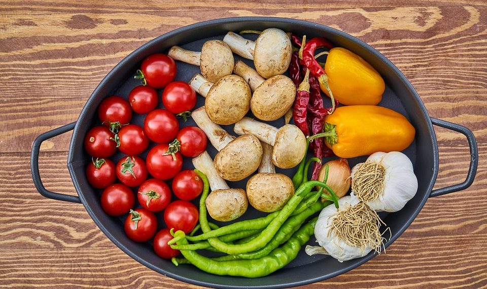 Fresh vegetables like tomatoes, mushrooms, and peppers in an oval pot.