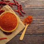 Bowl of chili powder with dried peppers on wooden table.