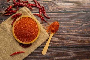Bowl of chili powder with dried peppers on wooden table.