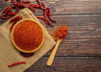 Bowl of chili powder with dried peppers on wooden table.