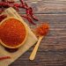 Bowl of chili powder with dried peppers on wooden table.