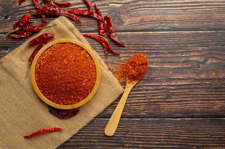 Bowl of chili powder with dried peppers on wooden table.