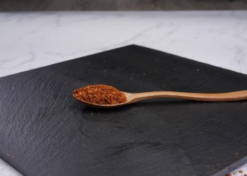 Wooden spoon with paprika on black slate board.